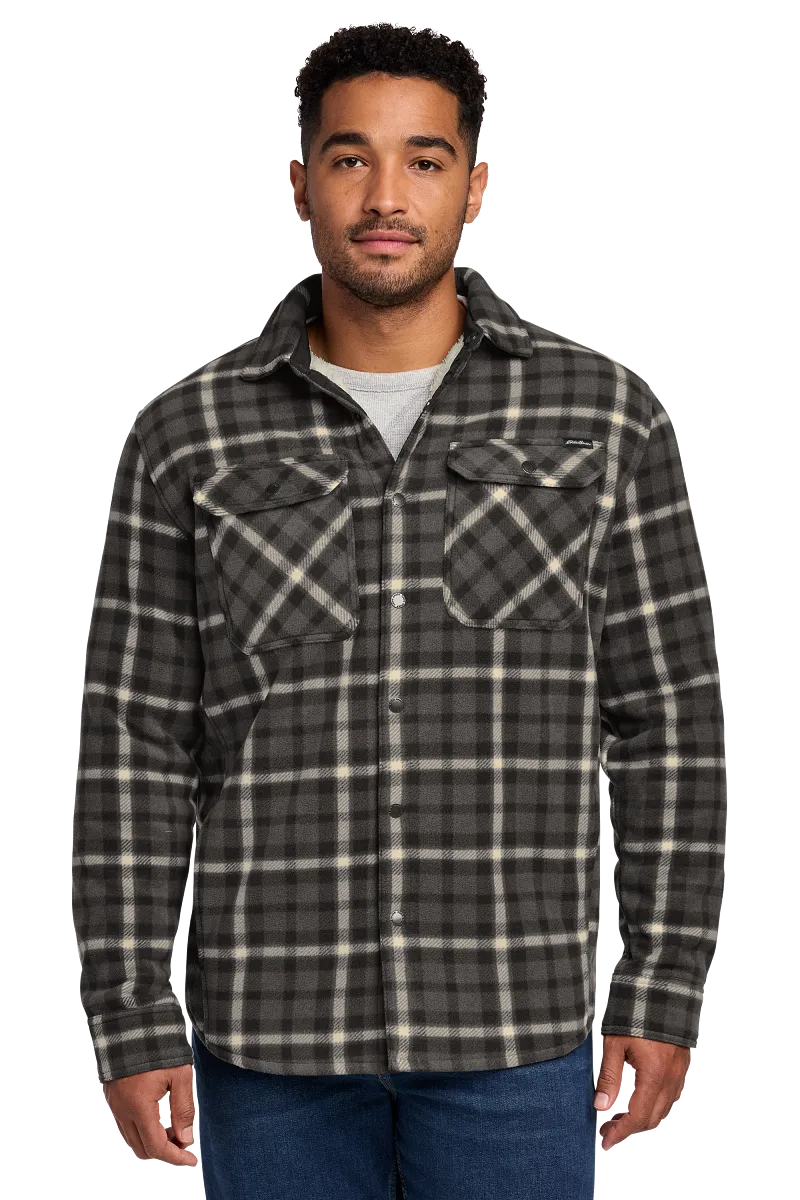 Man wearing the Eddie Bauer Woodland Shirt Jac in charcoal plaid flannel, buttoned with two chest flap pockets, paired with a heather gray t-shirt and jeans.