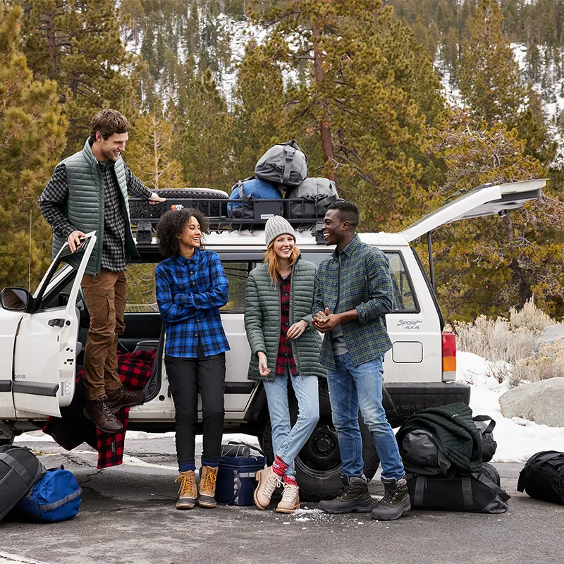 Group wearing Eddie Bauer plaid flannel shirts and quilted vests, loading gear onto an SUV at a snowy trailhead