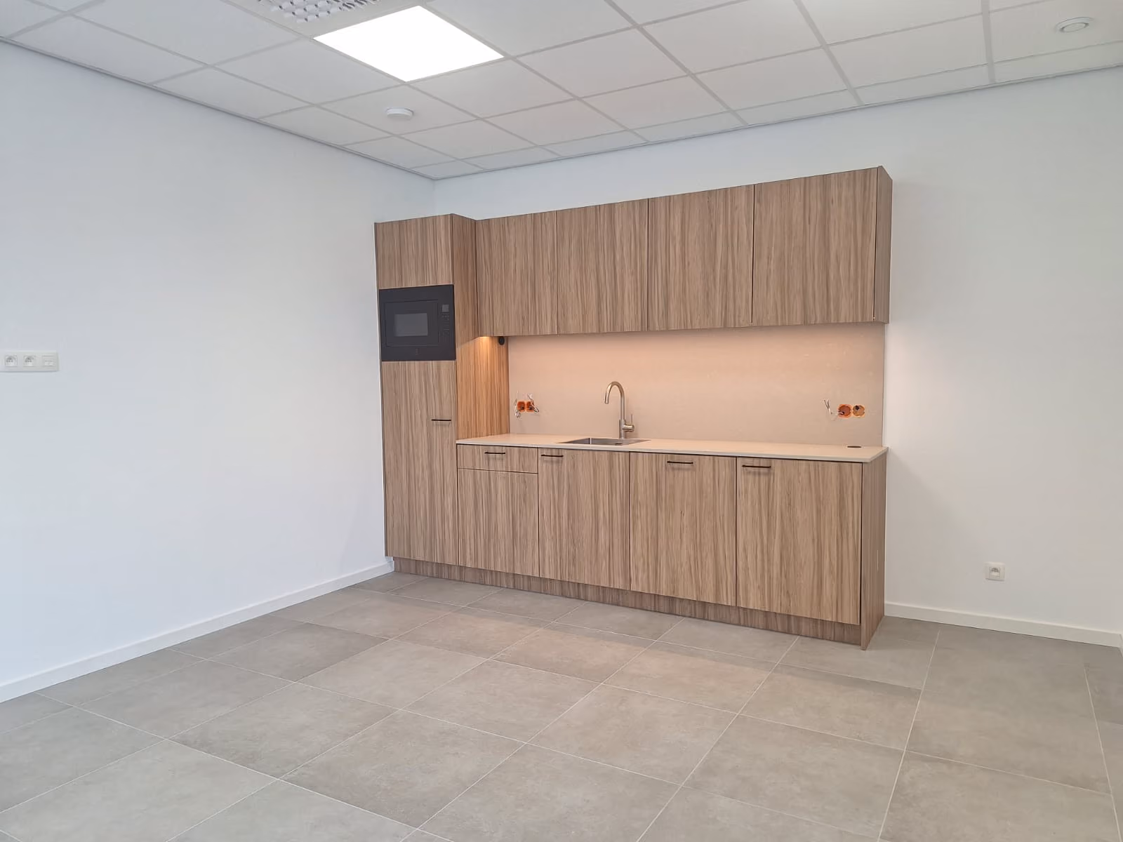 Kitchenette in houtlook met inbouwoven in een lichte ruimte met systeemplafond