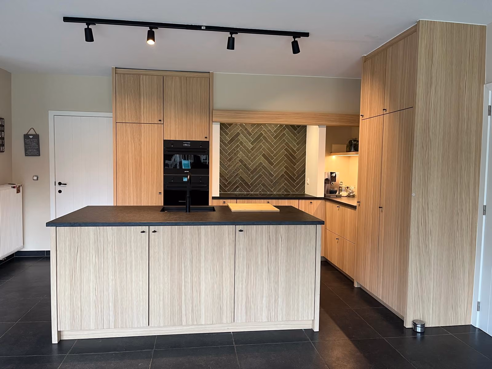 Keuken met kookeiland, hoge kasten in houtlook en zwarte werkbladen