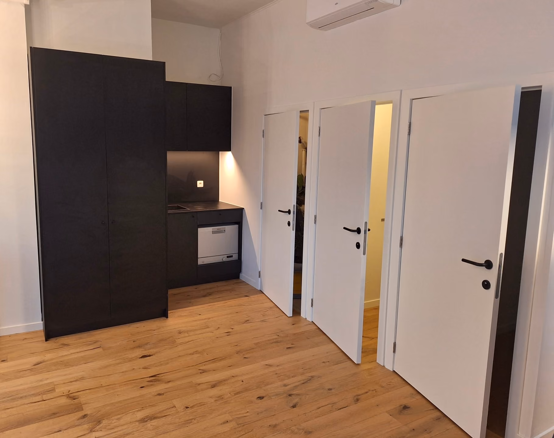 Ruimte met eikenhouten vloer, zwarte maatwerkkast, kitchenette en witte binnendeuren