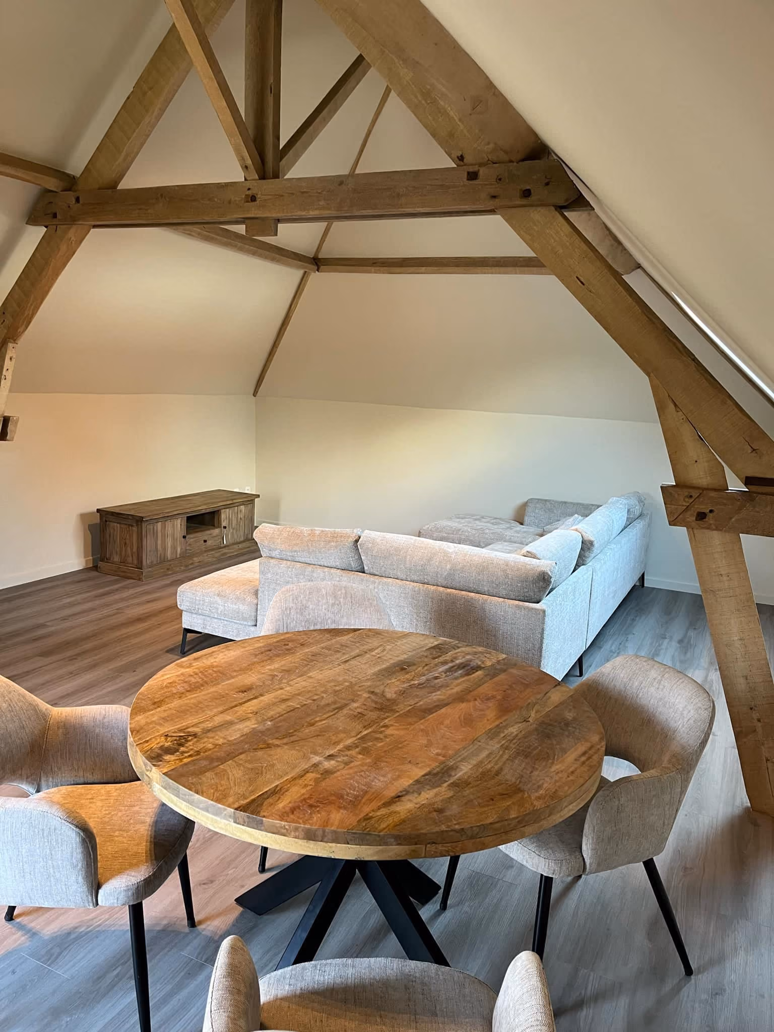 Zolderruimte met zichtbare houten dakspanten, ronde eettafel en zithoek