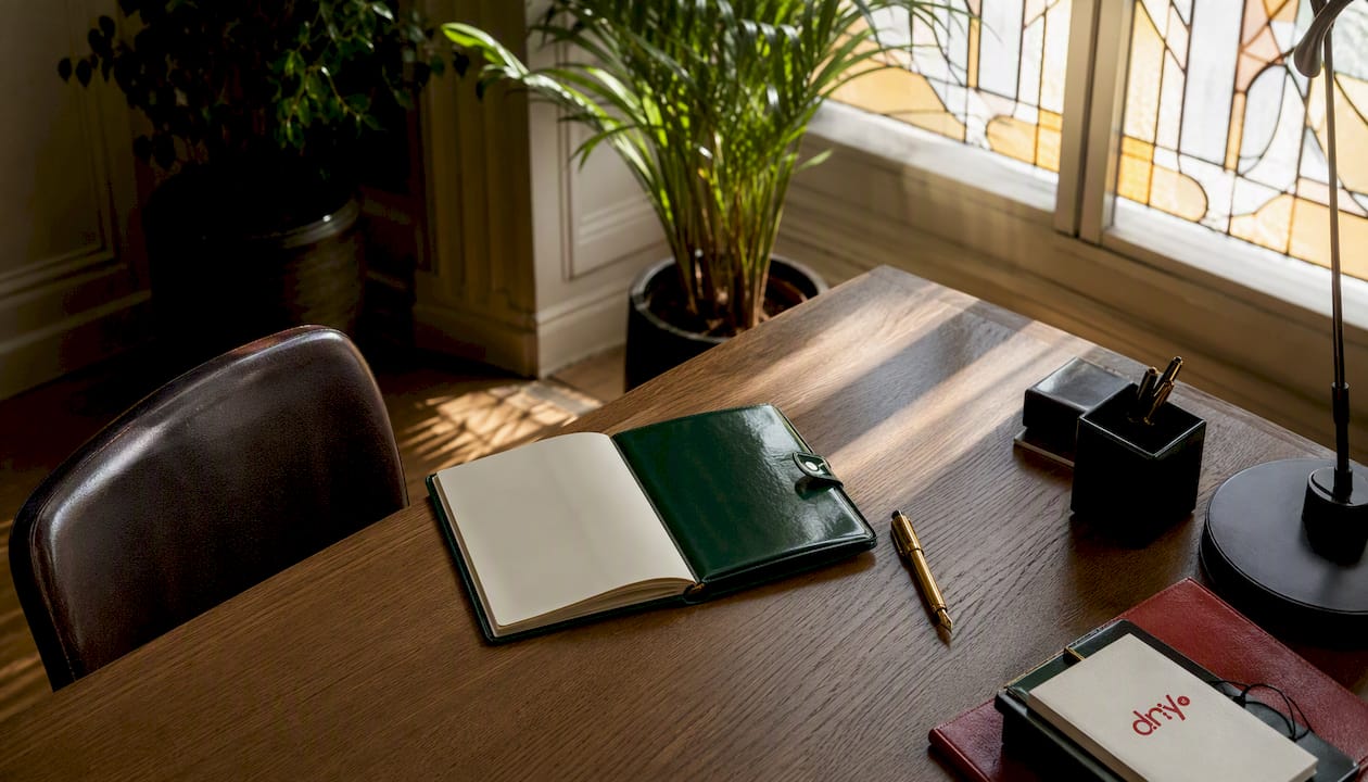 Un carnet en cuir accompagné d’un stylo posé sur un bureau en bois.