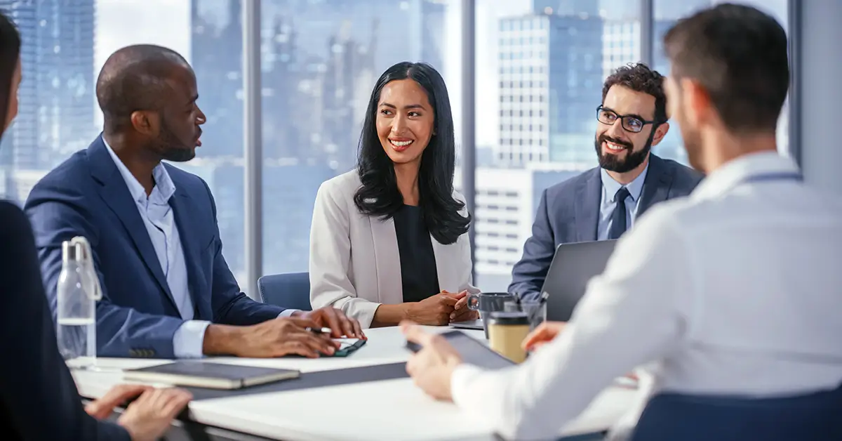Diverse business team in formal attire discusses strategy in a modern office, reflecting CISO-level collaboration on secure agentic AI adoption.