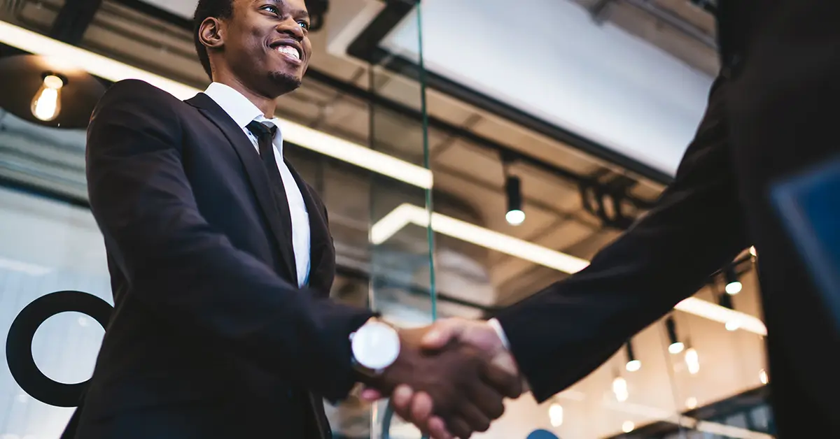 Business professionals in suits shaking hands in a modern office, symbolizing the Leah and PwC UK partnership on Agentic Operating Models.