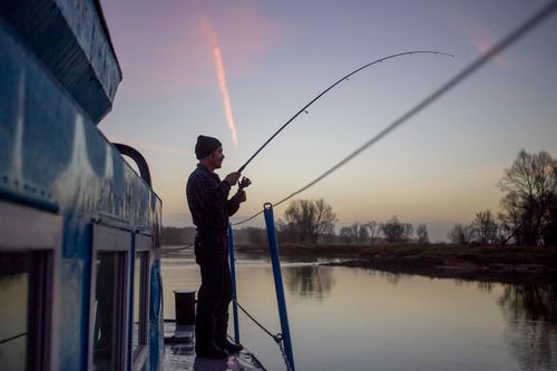 River sailor Zbigniew Laskowski fish from an anchored ship's deck, during transport cruise on the Odra.