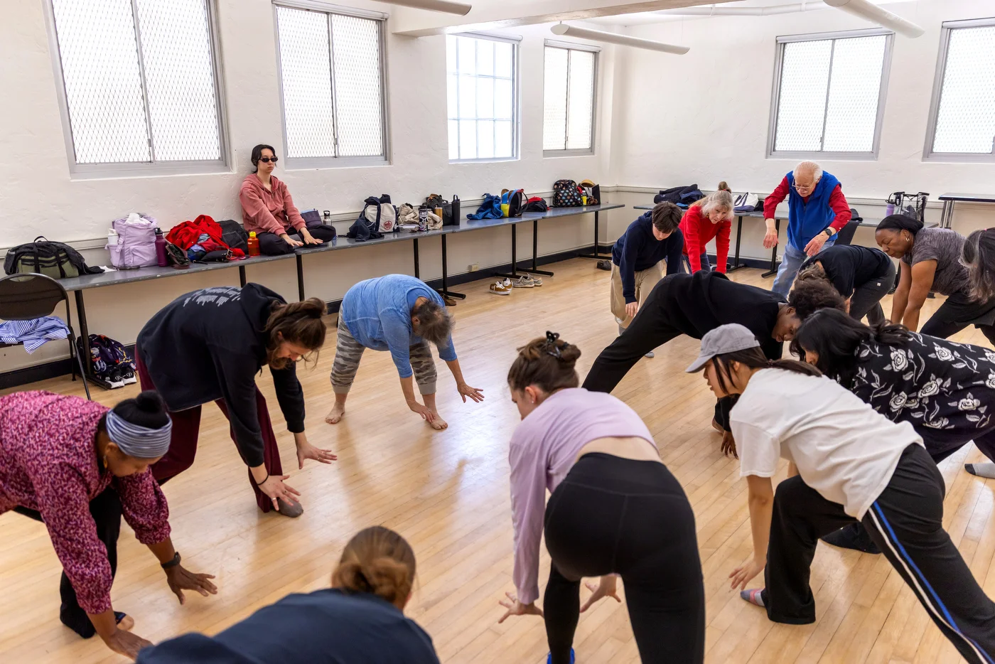 Dancers warming up in another USF studio, sunlight filtering through windows, wooden floors echoing the dancers movement.