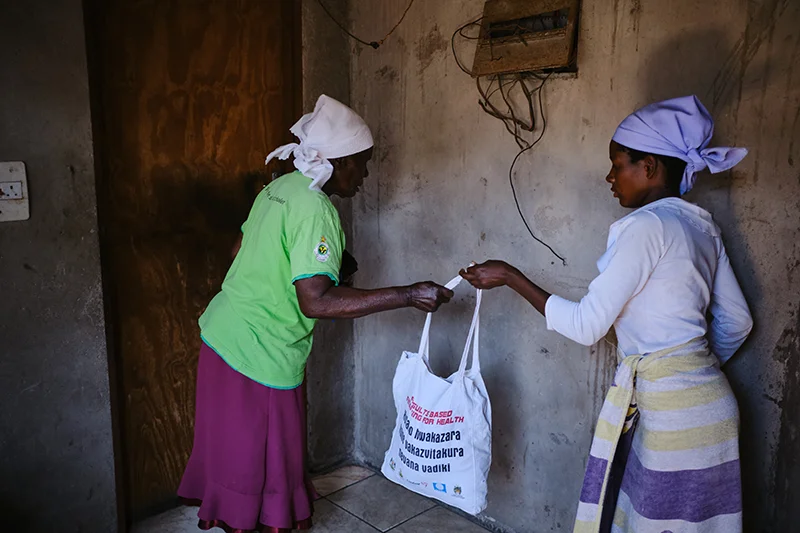 Shelta Nhengo, 75, inside her house in Mbare township receives her daily carry bag from Chipo Mabiye, 22.