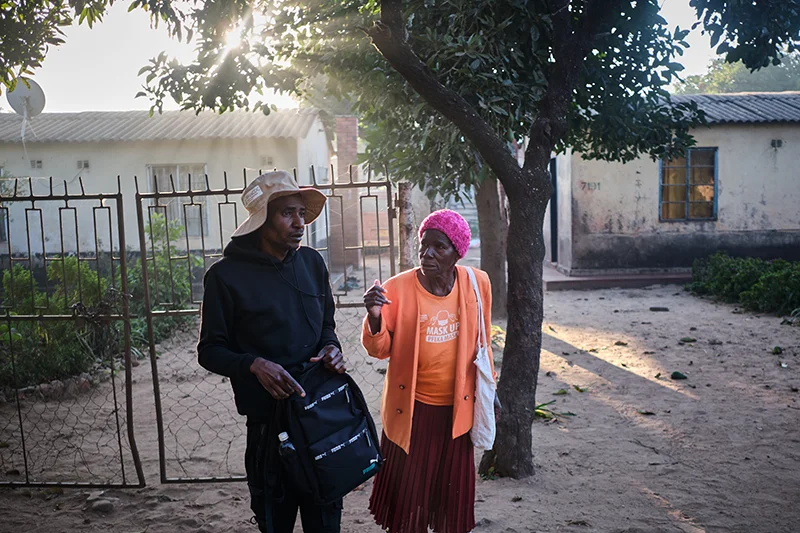 Shelta Nhengo, 75, talks to a colleague outside a house in Mbare township as they head out early morning.