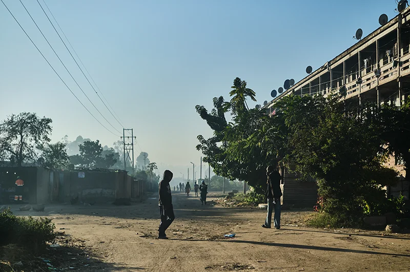 People walk the street amid a cloud of smoke near hostels in Mbare. 