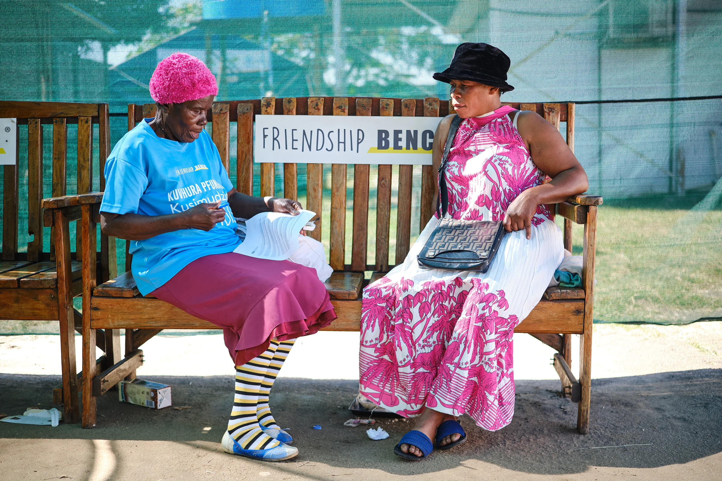 Shelta Nhengo, 75, interacts with Maidei Handiseni, 47 a resident and vendor on one of the Friendship Benches deployed at Mbare Hostels Clinic. Maidei Handiseni, a 47-year-old entrepreneur, provides insights into the impact of the post-COVID-19 pandemic on her second-hand clothing vending business.