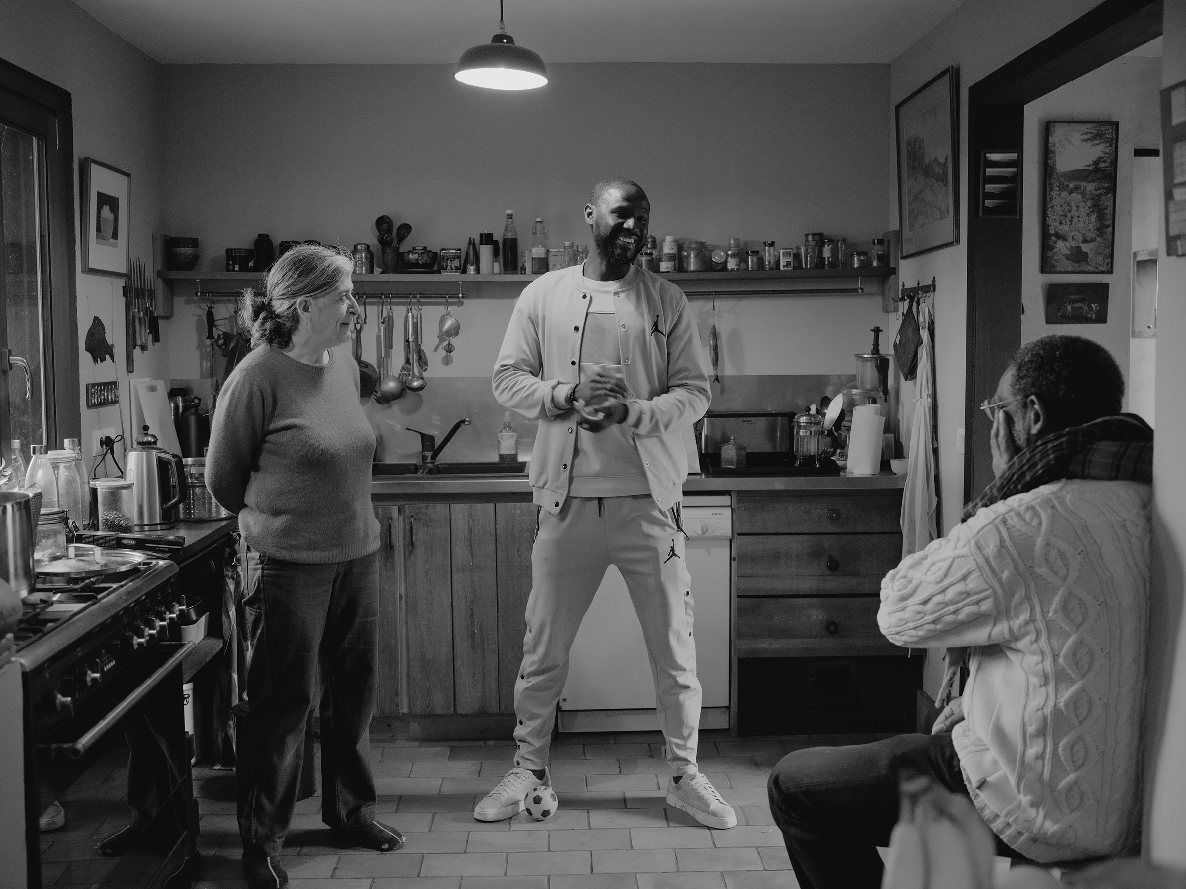 Arianne, Alhassane, and Valéry share a moment in the kitchen, catching up over lunch as Arianne prepares the meal.