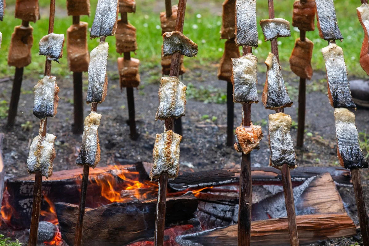 Salmon cooks over the fire as part of the day’s traditional food preparation. The image reflects how food practices carry cultural knowledge, memory, and connection to community.