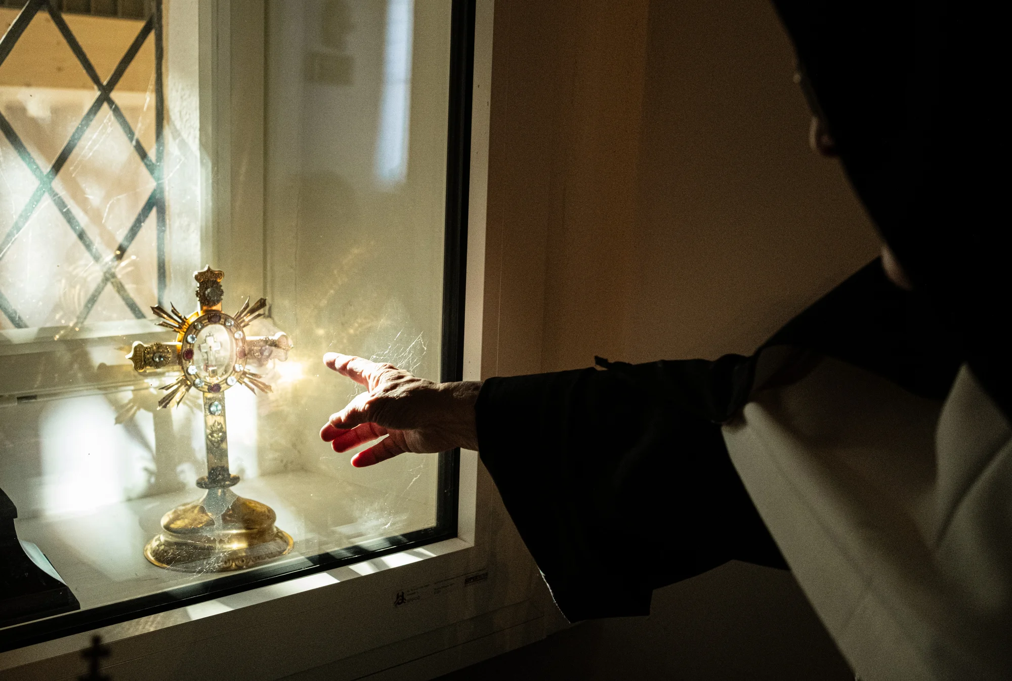 Sister Rita (82) points to a monstrance, protected behind a panel of glass which is miraculously lit by direct sunlight at almost exactly noon on the last day of the year through a small window several meters behind, Elsbethen, Austria, Dec 31, 2025.