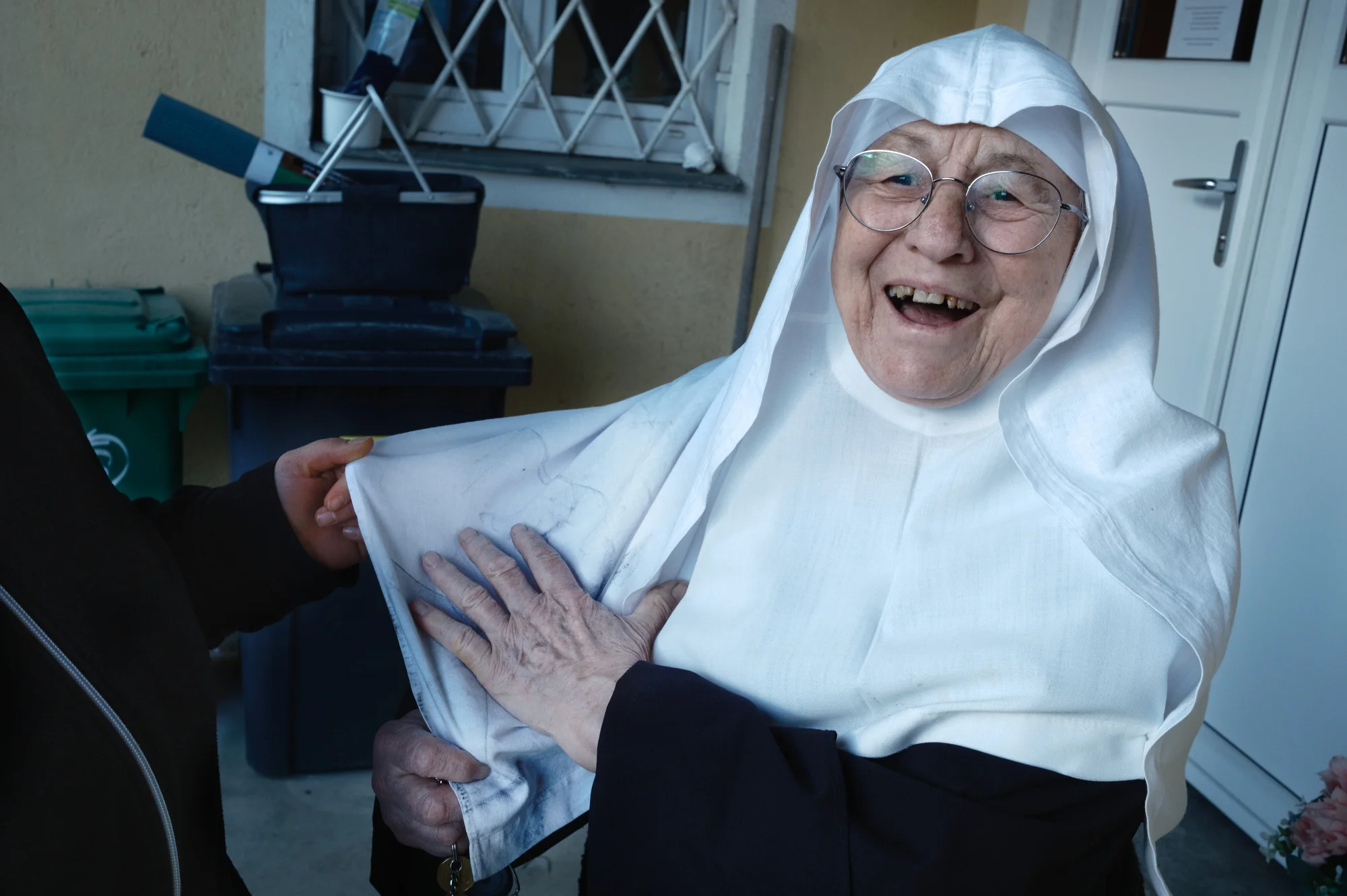 Martina, one of the Sisters full-time caretakers, holds up Sister Rita's habit while Sister Rita laughs, a little embarrassed, trying to cover up that she got her white habit dirty after a walk in the garden.