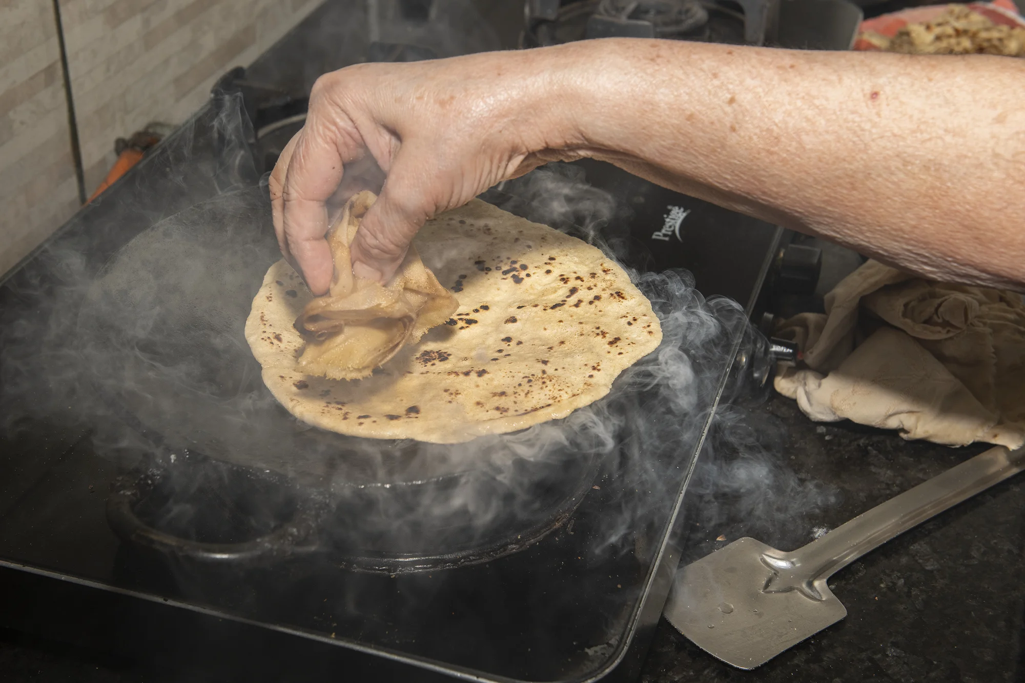 Vandana G Talreja, 69, uses a damp cloth to press a chapati as it puffs on a hot tawa in her kitchen in Bangalore, India, on Aug. 23, 2026.
