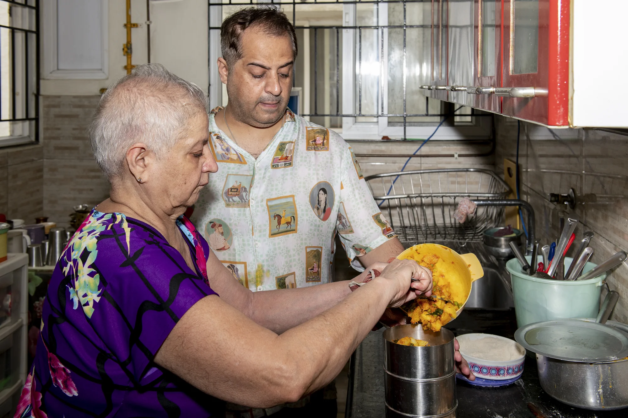 On Aug. 23, 2026, Vandana G Talreja, 69, fills a tiffin box for delivery in her kitchen. Her son, Deepak, manages deliveries to customers.