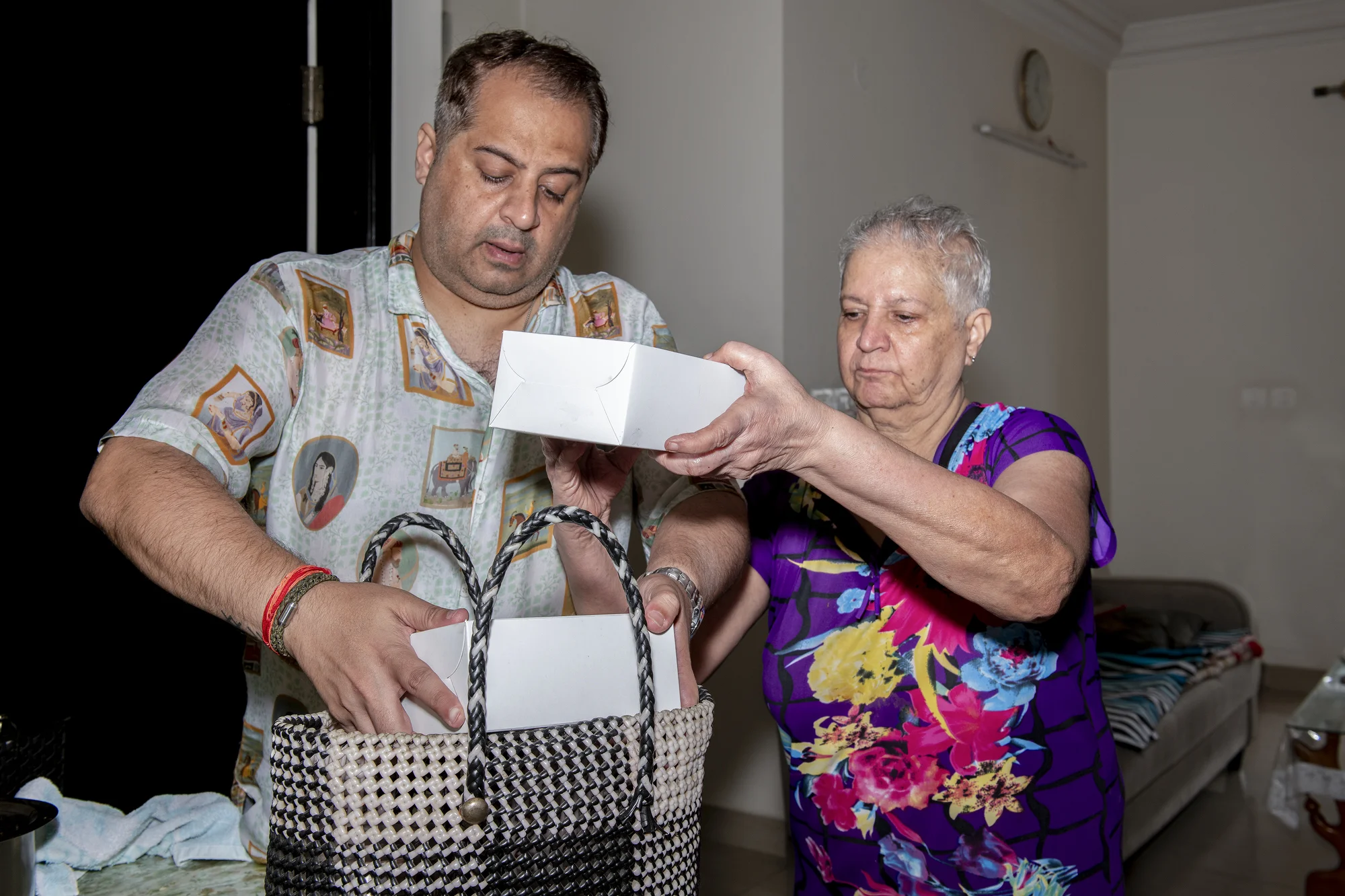 Vandana G Talreja, 69, guides her son, Deepak, as he places paper food boxes inside a delivery bag.