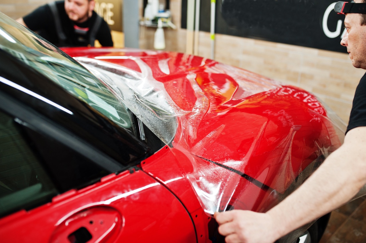 Two paint protection film installing technicians adding PPF to a vehicle's hood