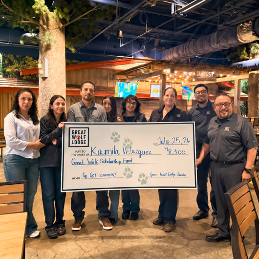 Scholarship recipient posing with Pack Members and a large check.