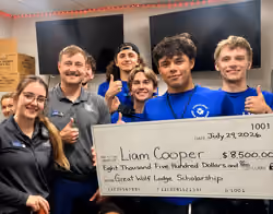 Liam Cooper holding a scholarship check for $8,500 with his Pack behind him