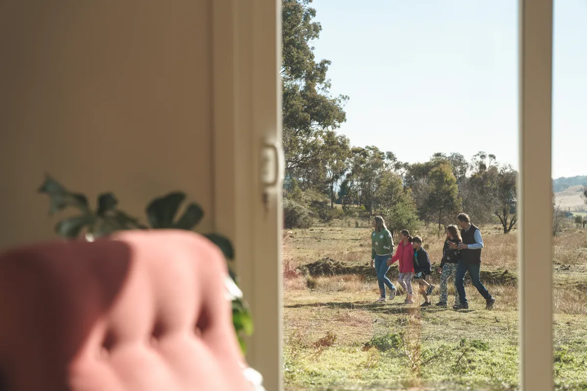 The family walks together outside, you can see them through the glass sliding doors in their home