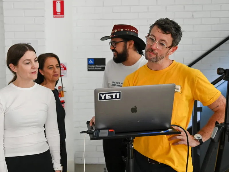 Four people standing around a laptop reviewing the images being taken of customers.