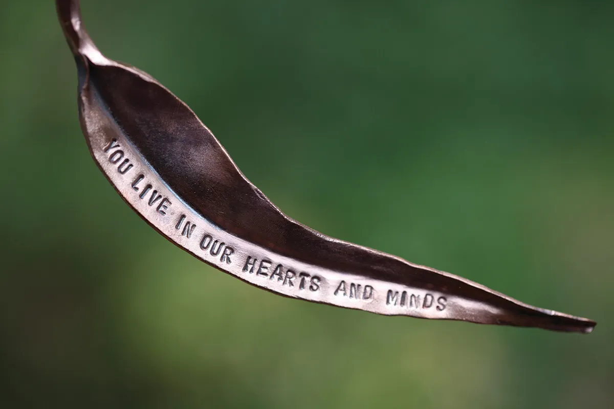 A metal leaf that says "You live in our hearts and minds"