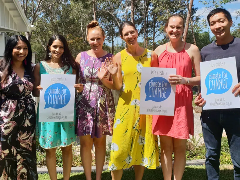 A group of people gather around outside smiling and waving. They hold signs that say "Lets create a climate for change"