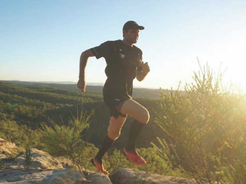 A man runs outside surrounded by nature, he jumps over rocks