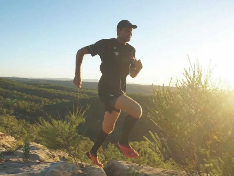 A man runs outside surrounded by nature, he jumps over rocks