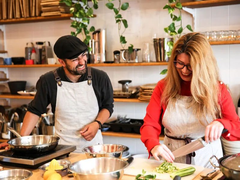 Two people are cooking together. They both smile and laugh at each other. 