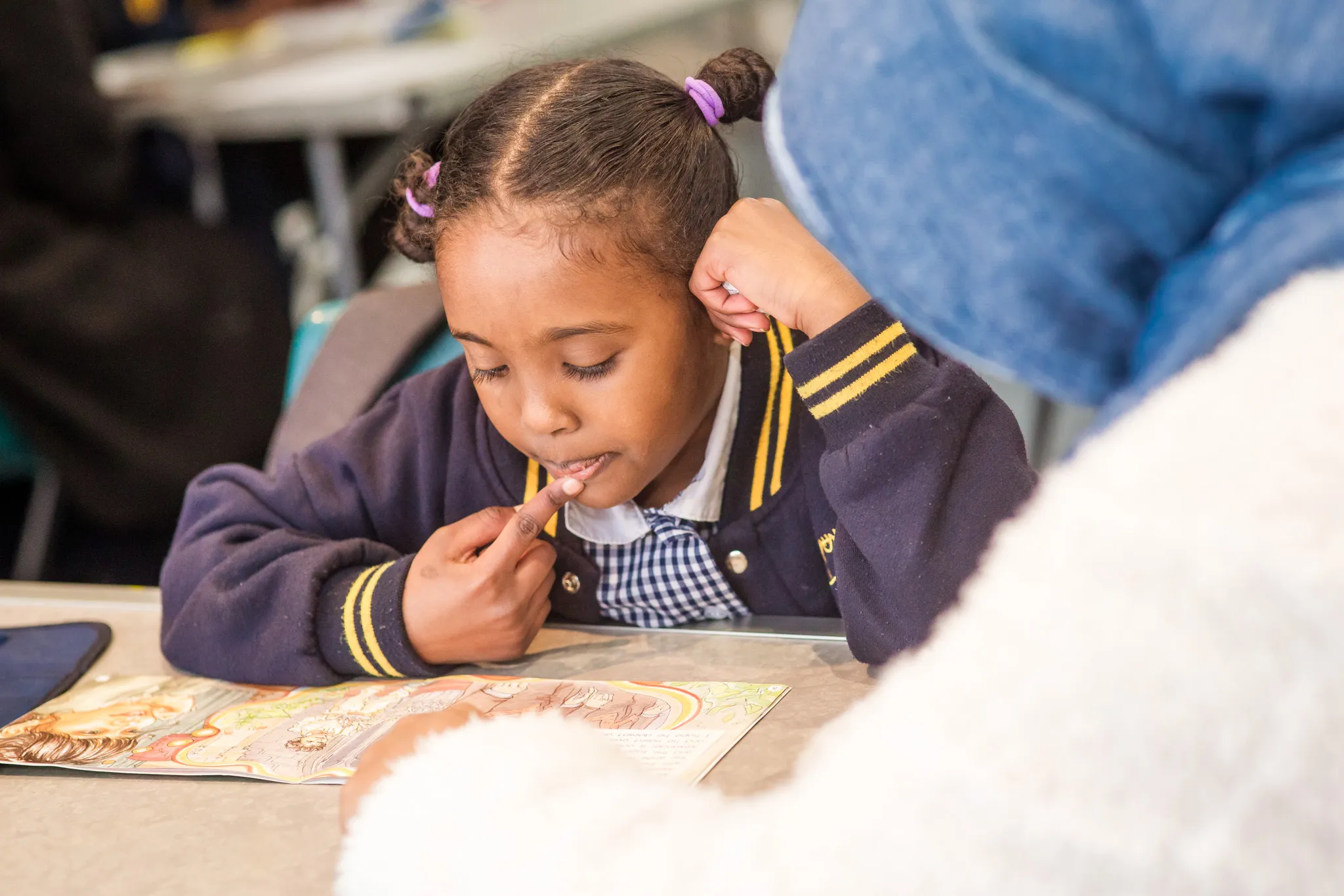 A child reads a book while a teacher assists them