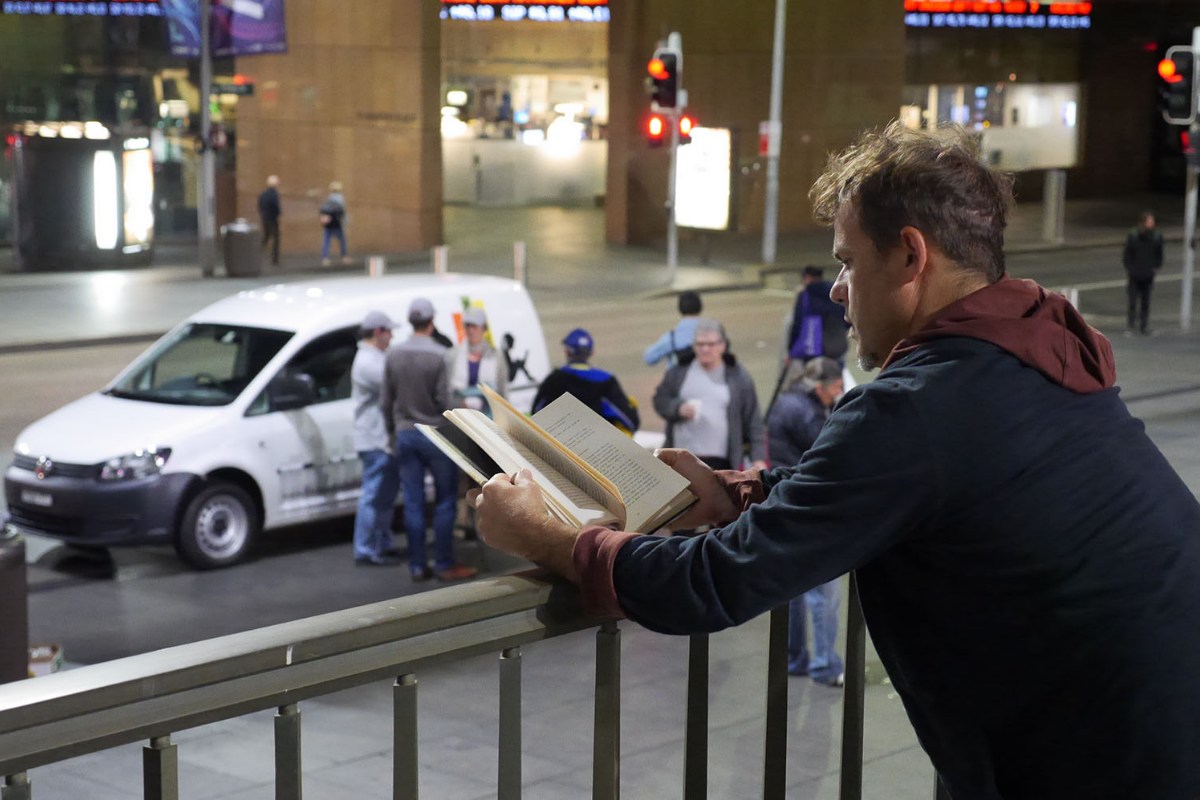 A man reads a book in a busy city at night