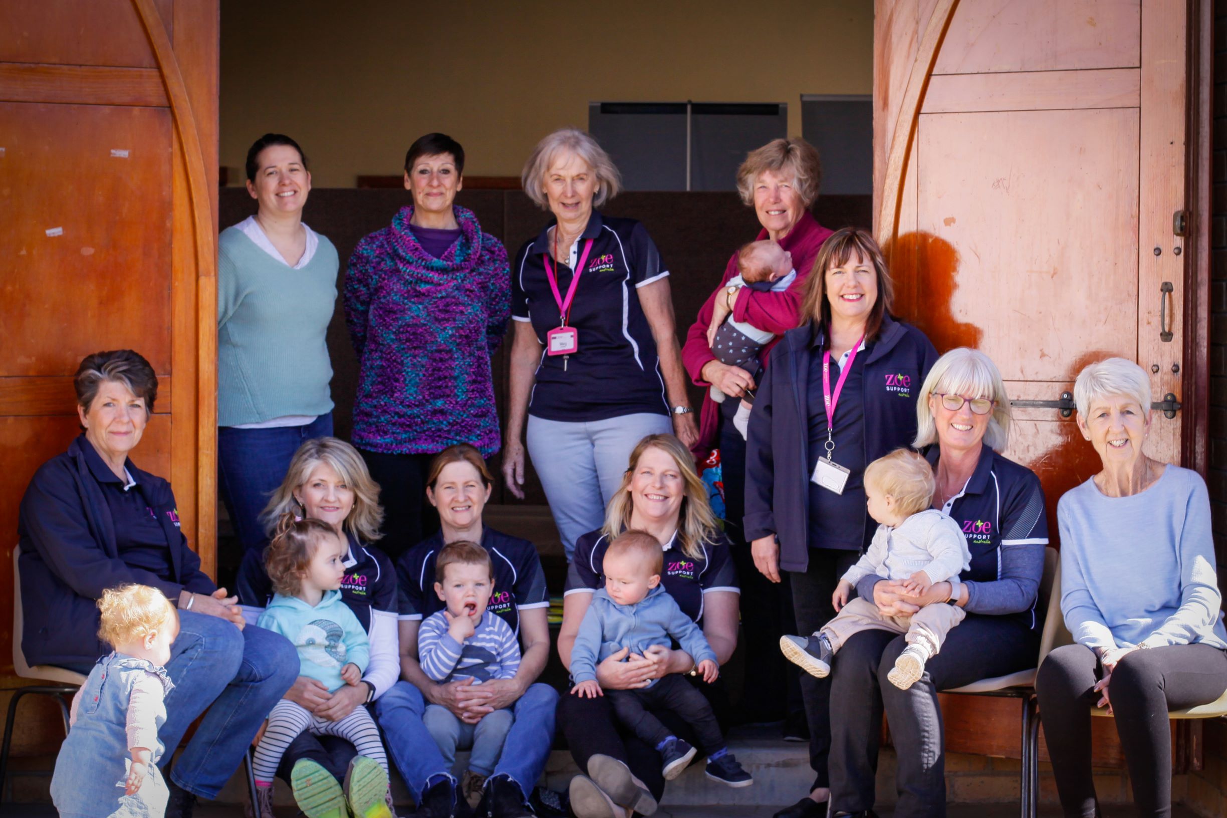 A group of woman stand and sit together. Some are holding babies and toddlers