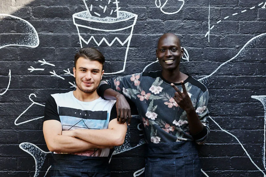 Two people lean against a painted mural. One does the peace symbol