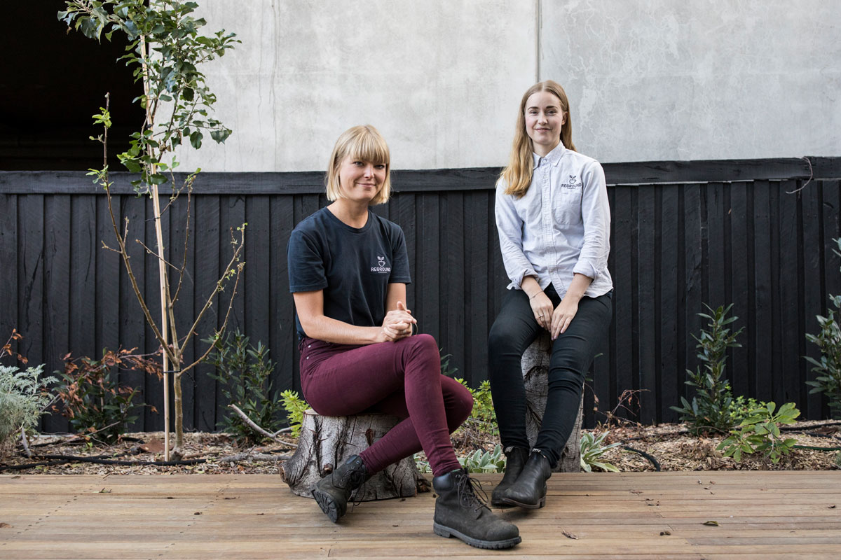 Two women sit on wooden tree stumps outside