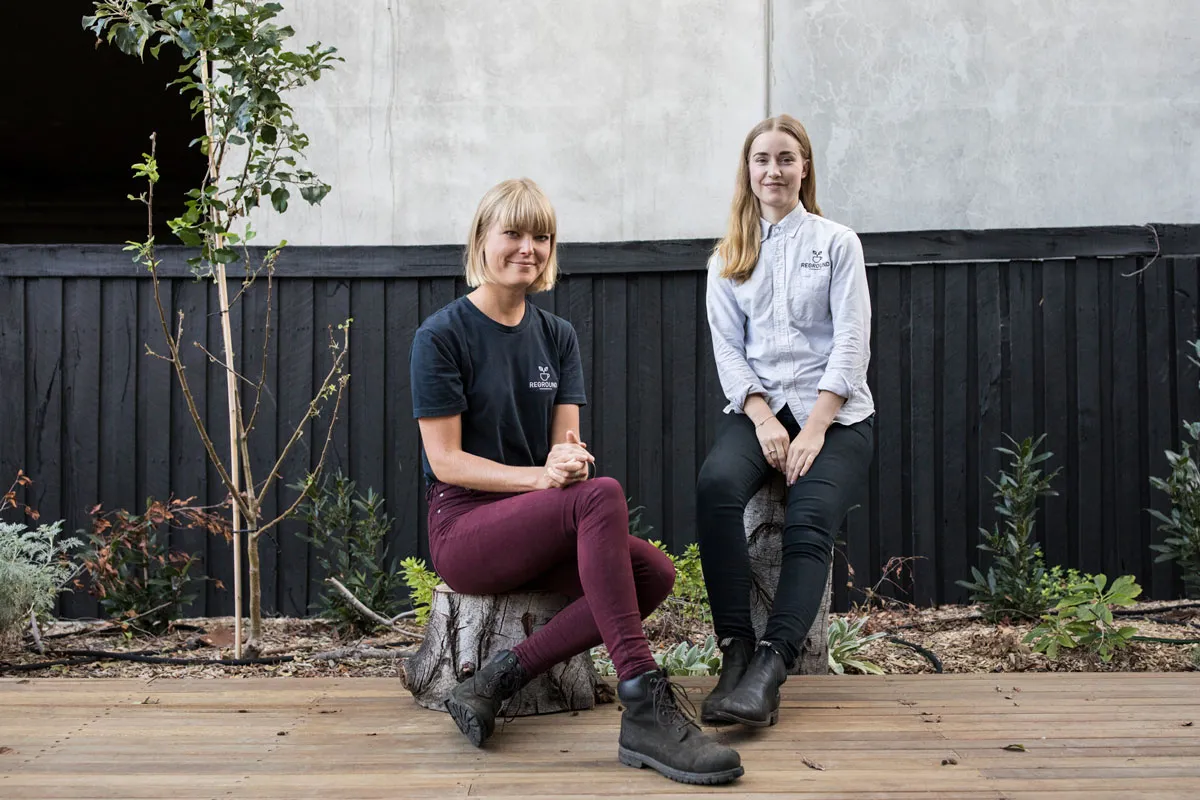Two women sit on wooden tree stumps outside