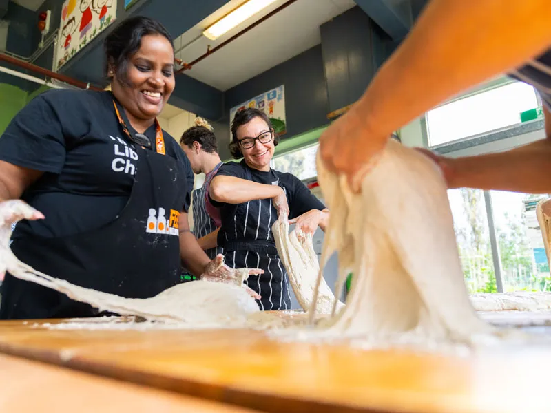 Three people knead dough in a kitchen