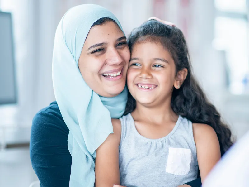 A woman holds her child, both are smiling