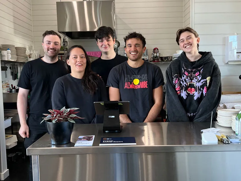 A group of people gather together behind the counter of a commercial kitchen