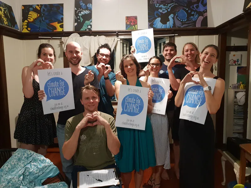 A group of people stand together and make heart shapes with their hands. Some hold signs saying "Let's create a climate for change"