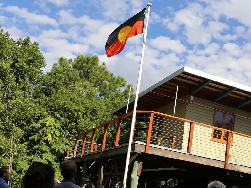 The First-Nations flag is raised up on a flagpole, next to a house. People gather around