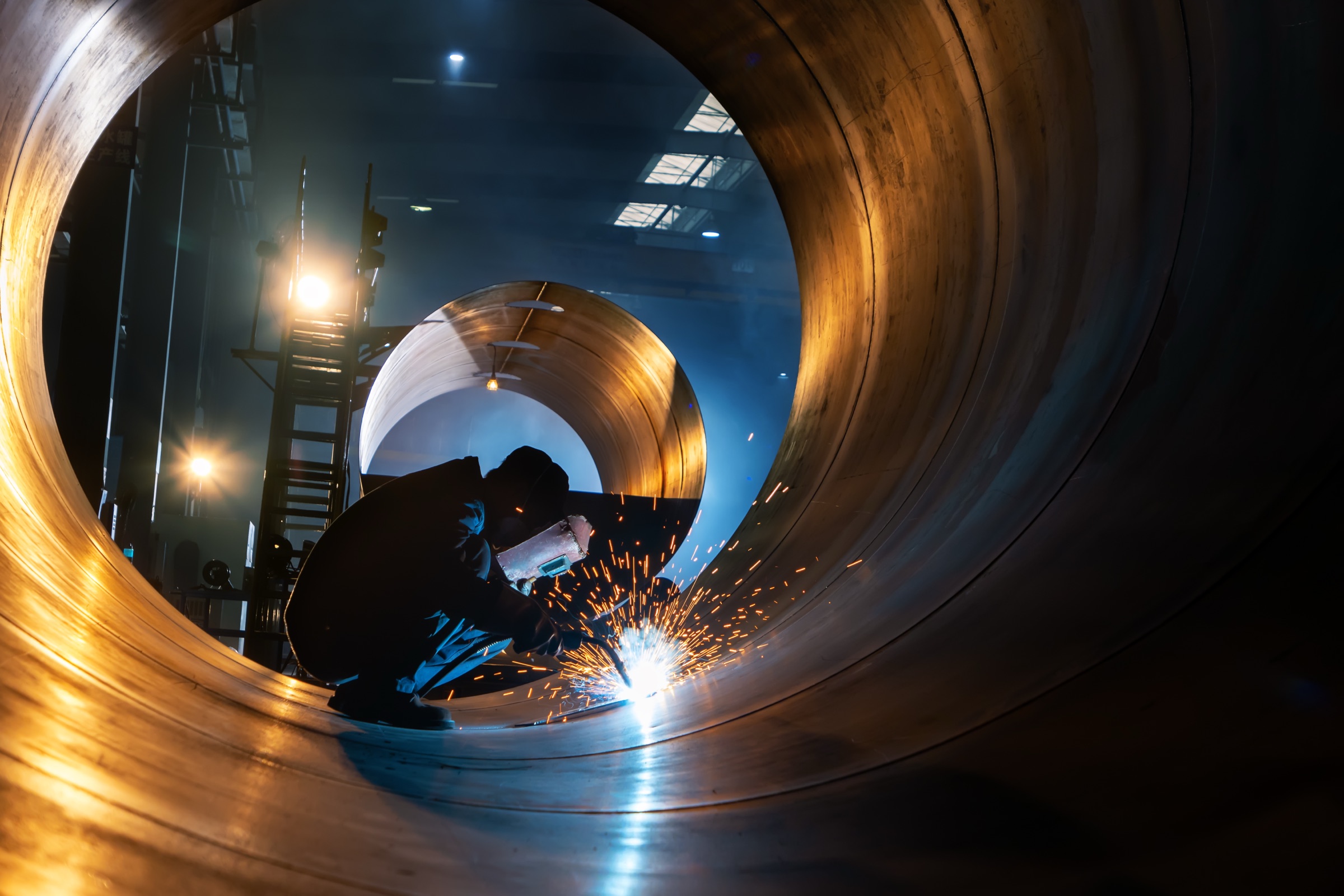 Welder joining a large-diameter rolled steel shell inside a fabrication bay