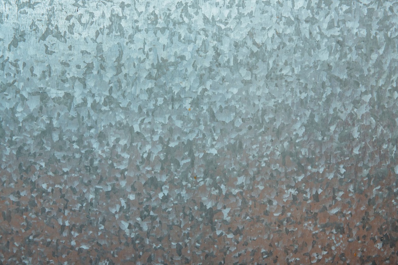 Galvanized steel sheet with a bright zinc spangle coating fading into rust and corrosion along the lower edge