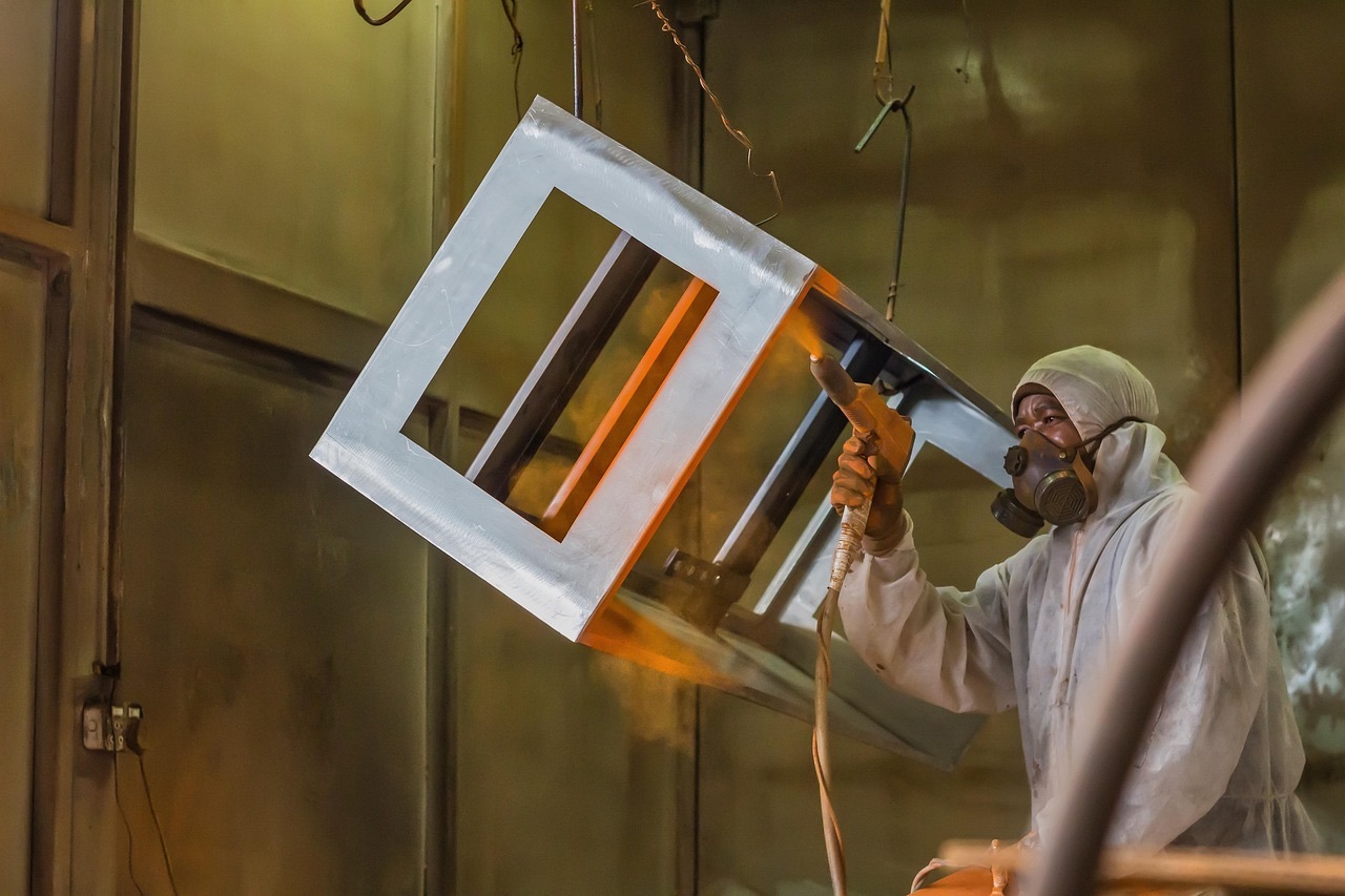 Worker in protective coveralls and respirator powder coating a metal frame inside a spray booth