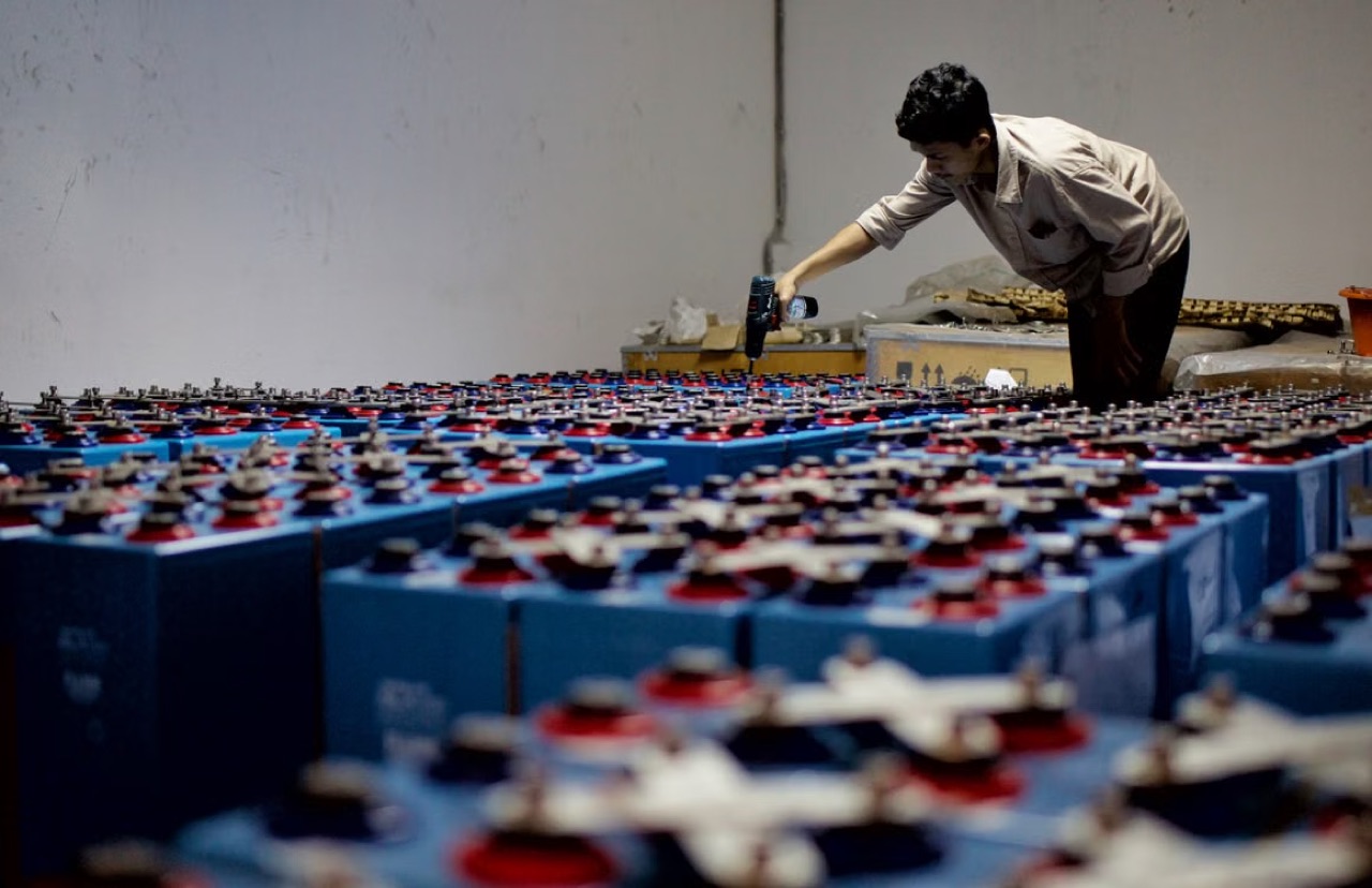 Worker inspecting rows of industrial batteries stacked in a warehouse