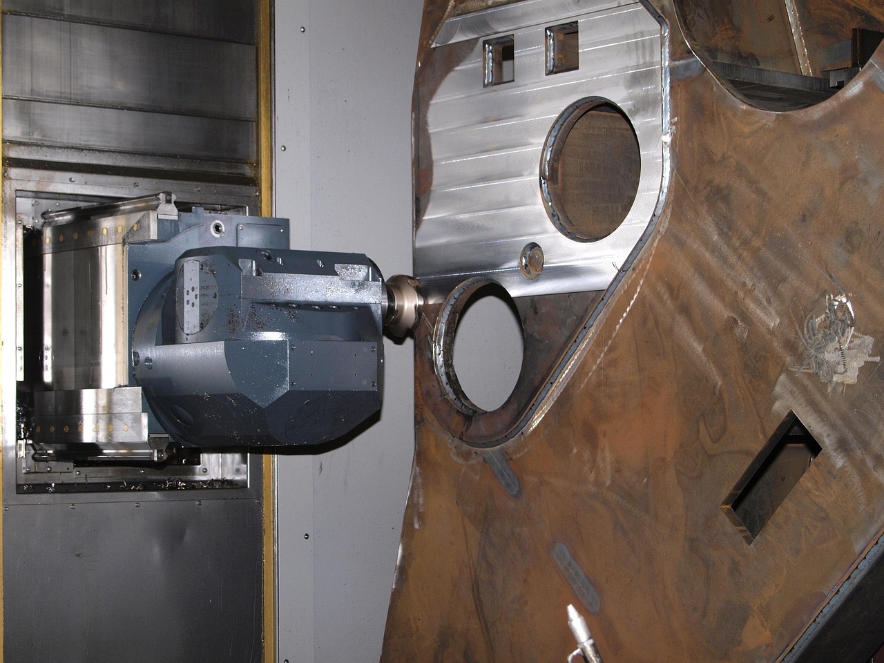 CNC machine spindle working on a large fabricated sheet metal panel with cutouts and welded flanges