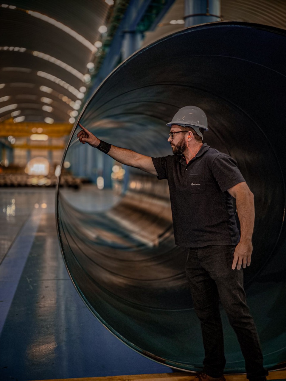 Engineer in a hard hat inspecting the inside of a large rolled steel pipe in a manufacturing plant