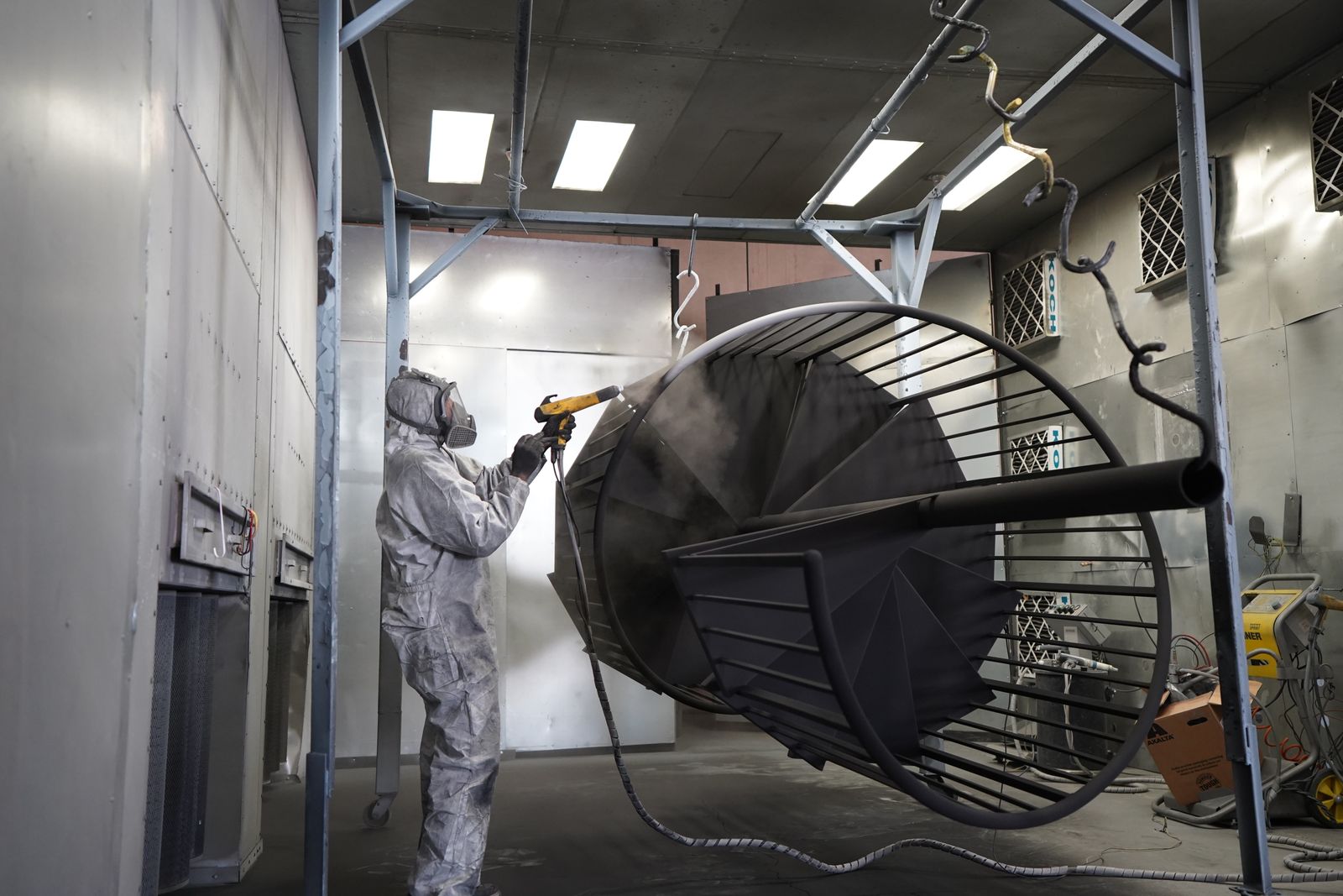Technician powder coating a metal structure inside an industrial finishing booth